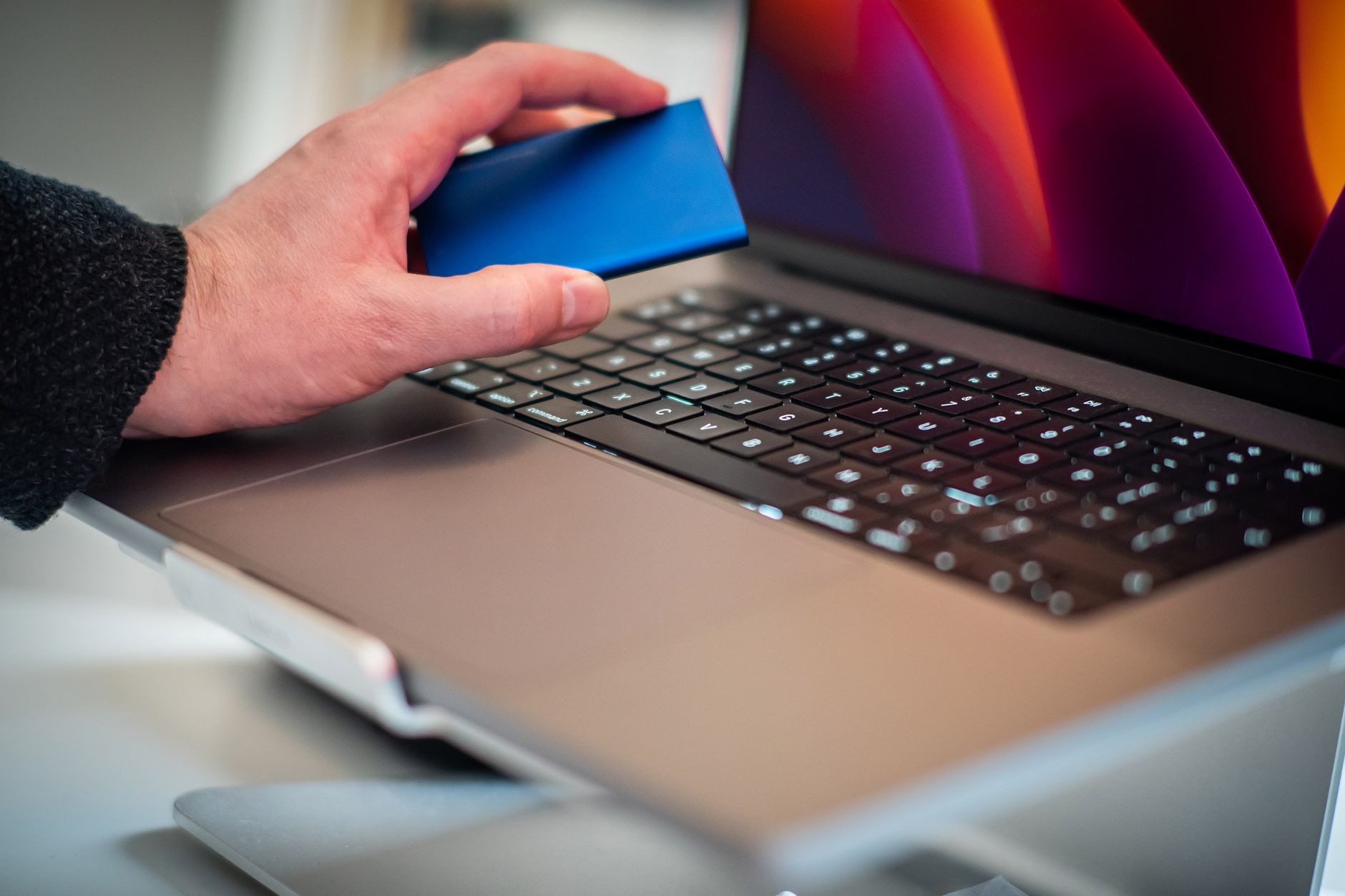 Main tenant un disque dur externe au-dessus du clavier d'un MacBook, prêt à le brancher pour une sauvegarde ou une récupération de données