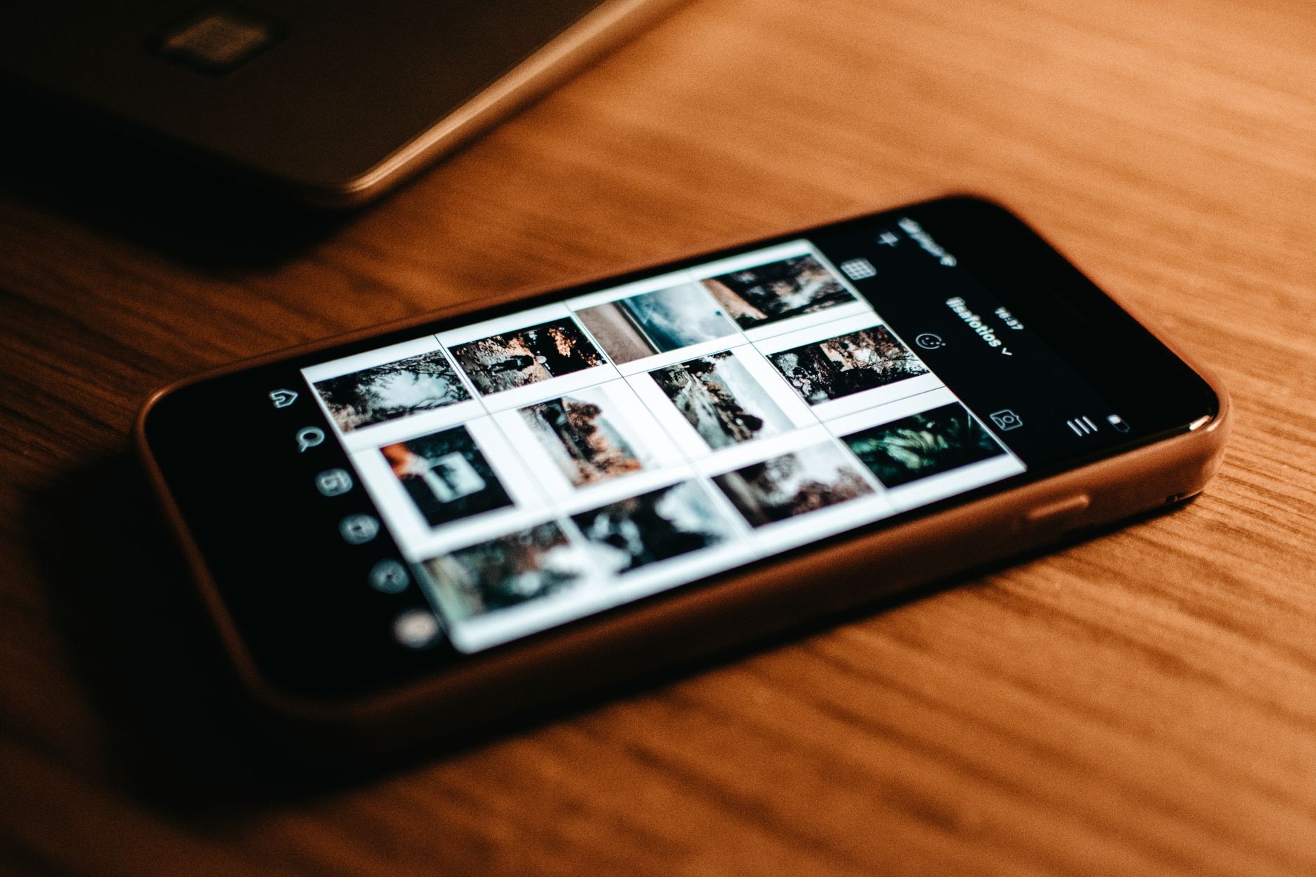 Gros plan sur un smartphone posé sur un bureau en bois, affichant une galerie de photos à l'écran