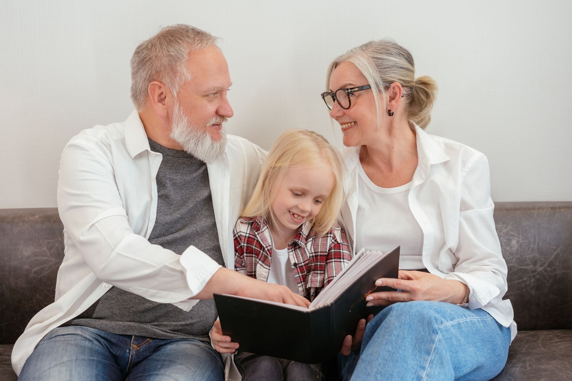 Des grands-parents et leur petite-fille souriants, regardant ensemble un album photo de famille